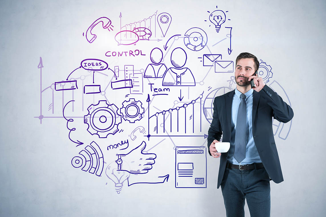 Young friendly businessman talking on smartphone and holding cup of coffee standing near concrete wall with business plan sketch on it.